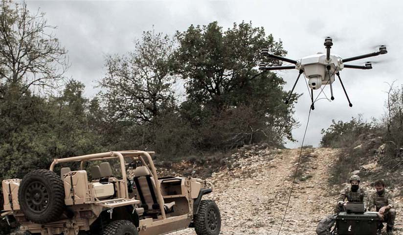 An army vehicle parked beside a tethered drone on the airfield.