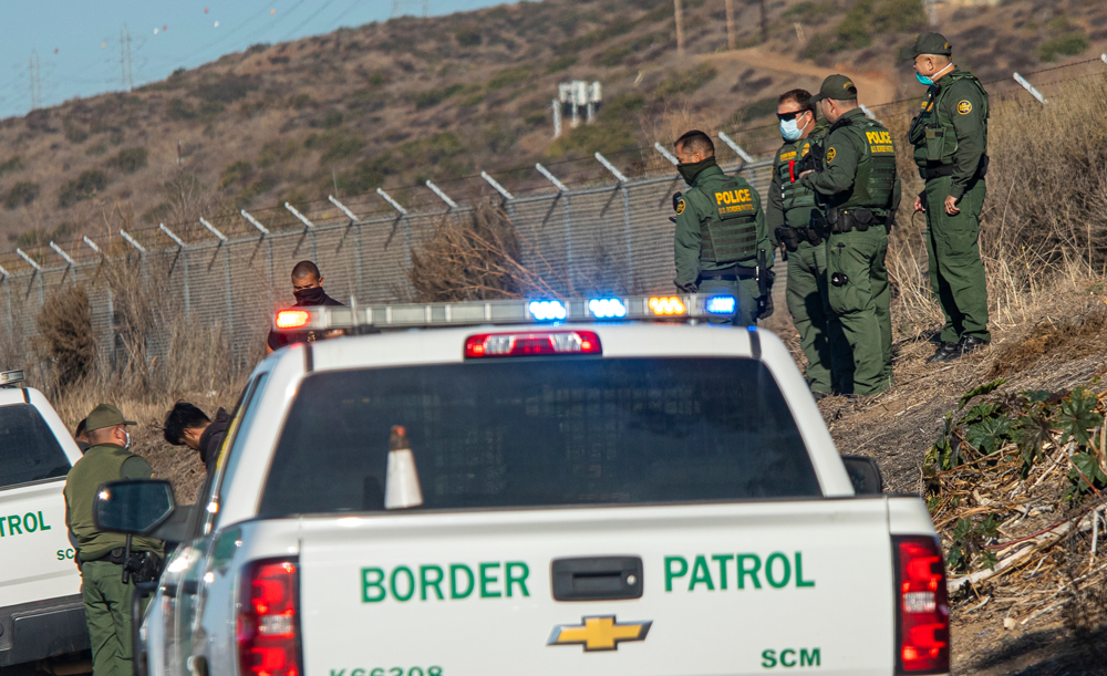 Border patrol agents stand near a fence with trucks