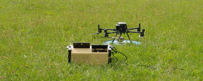 A tethered drone next to a tethered station in grassy field.