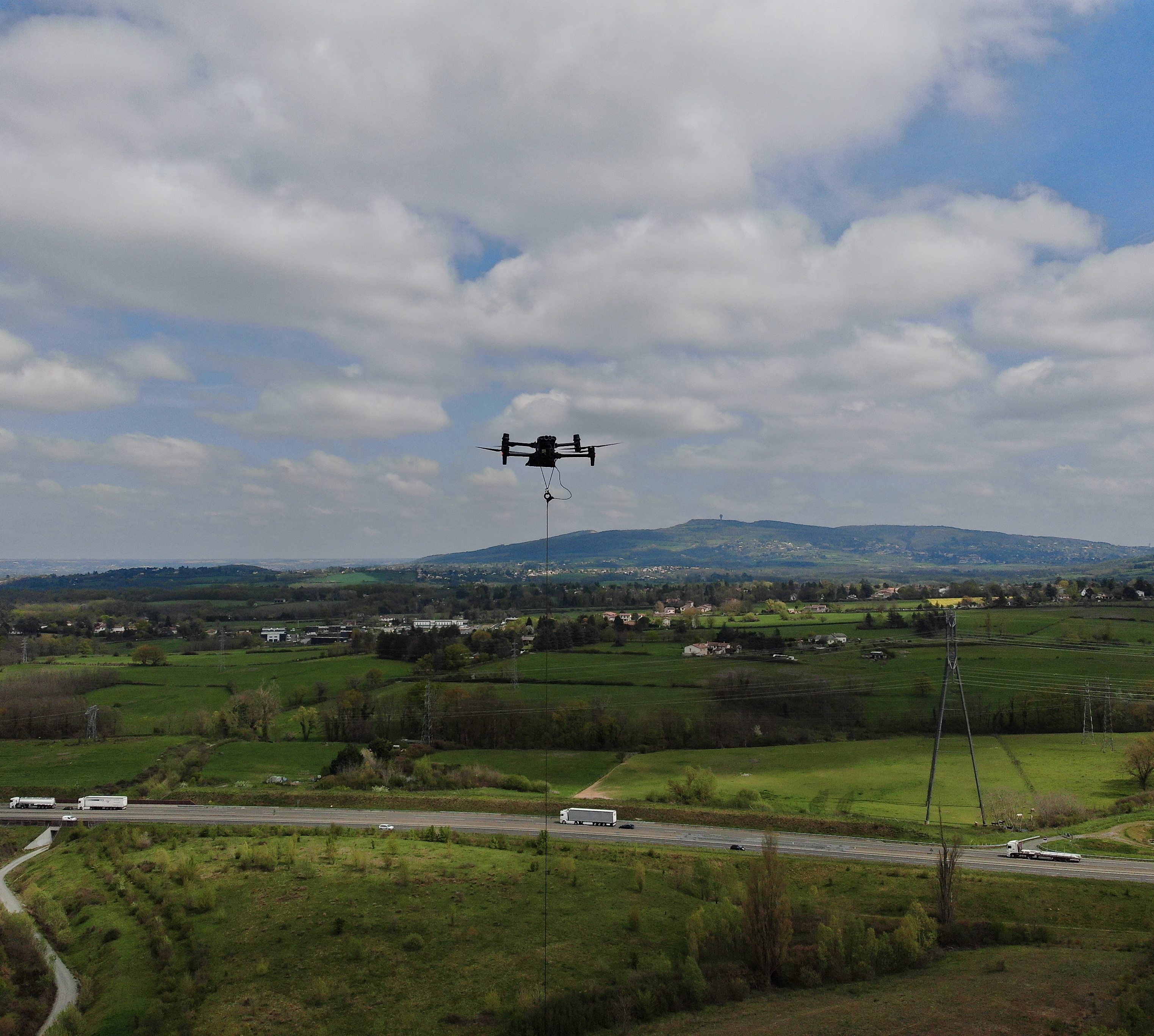 Tethered drone flying over a scenic landscape with hills and fields