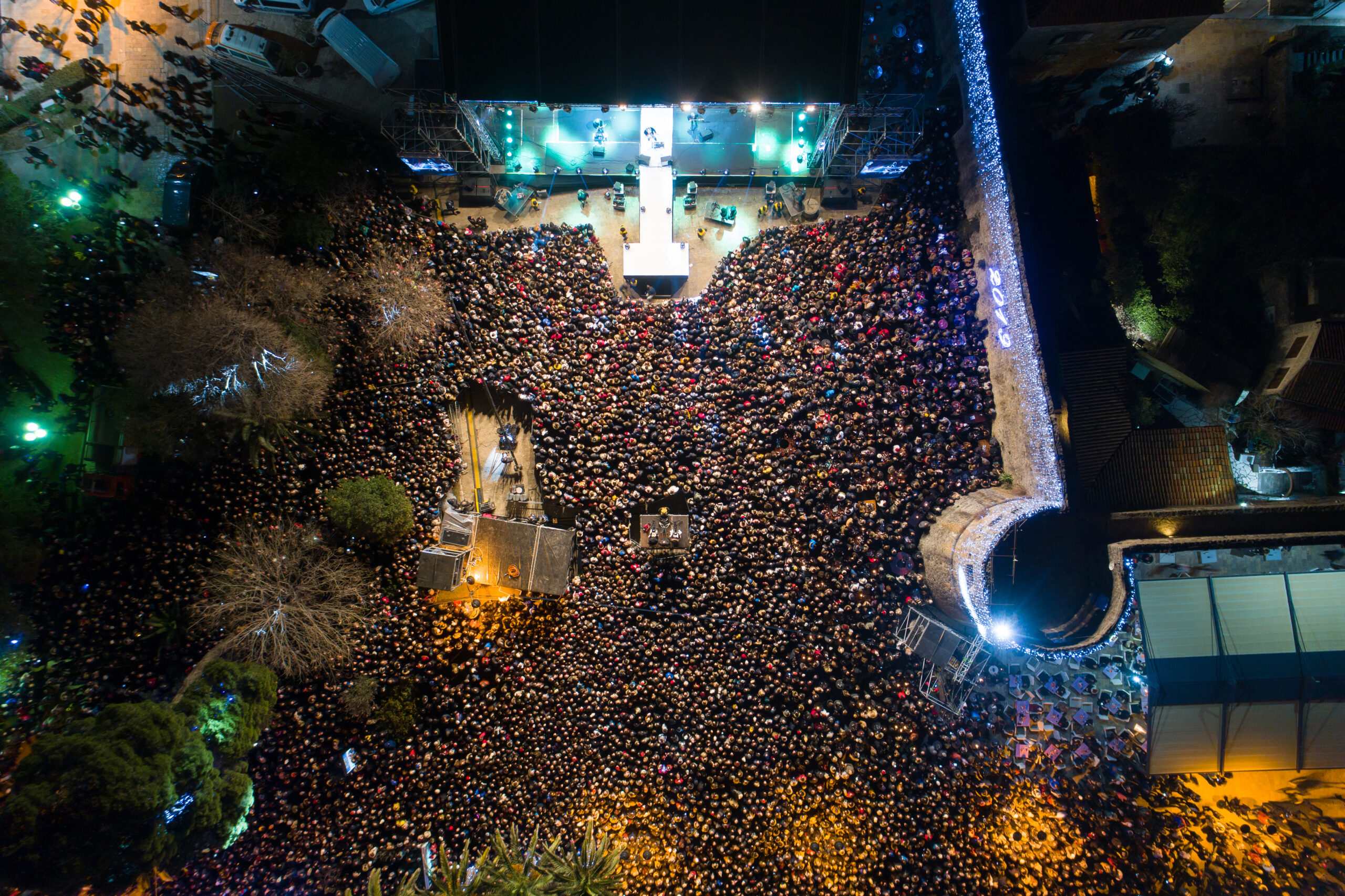 Aerial view of a large crowd attending a night event or concert with a stage and illuminated surroundings