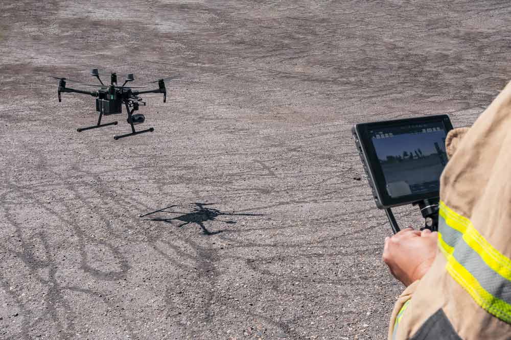 Firefighter operating a large rescue drone using a remote control tablet on a dirt field