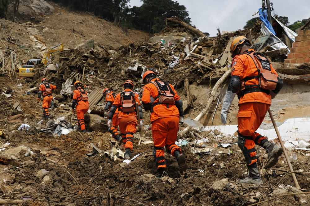 Rescue workers in orange uniforms climbing through rubble and debris after a landslide