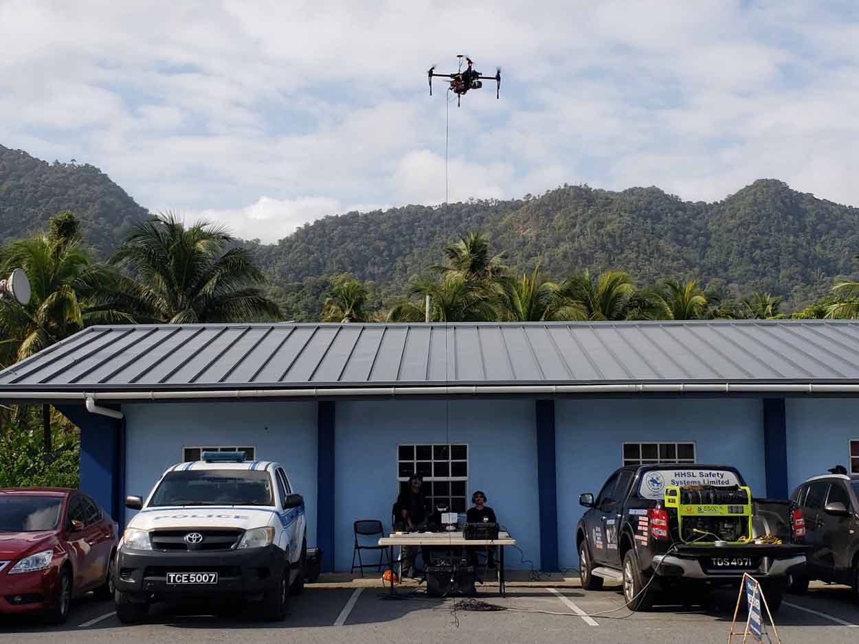 Police officers operating a tethered drone in front of a police station with mountains in the background